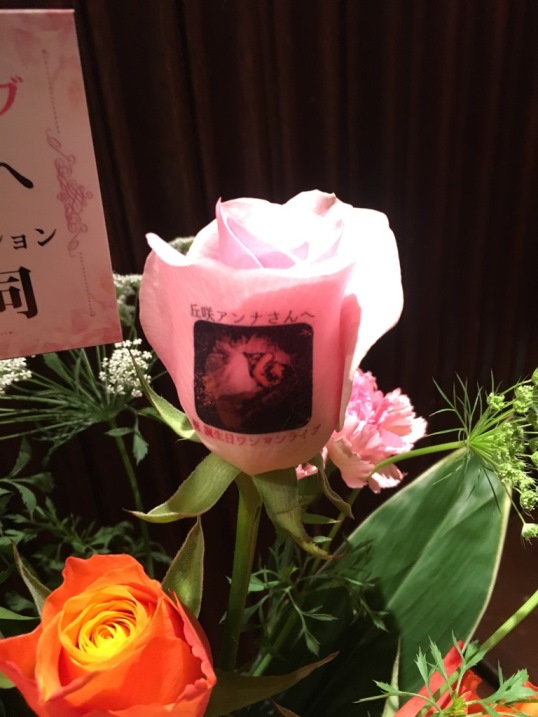 シンガーソングライター『丘咲アンナ』さんのバースデーライブに、応援している方々から贈られました、お祝いフラワーアレンジメントのバラに、このバースデーライブのイベント告知にのっている丘咲アンナさんのお写真と、お祝いメッセージをのせて♪